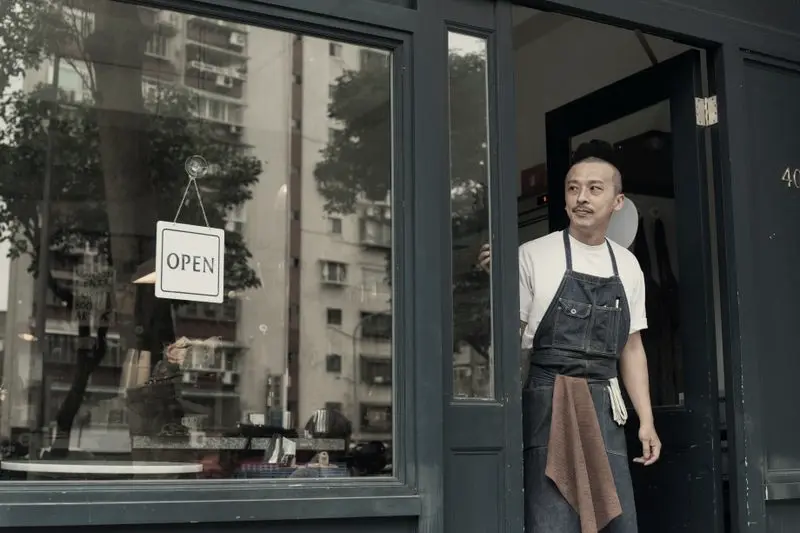 Dueño de una cafetería en la puerta, junto al cartel de abierto